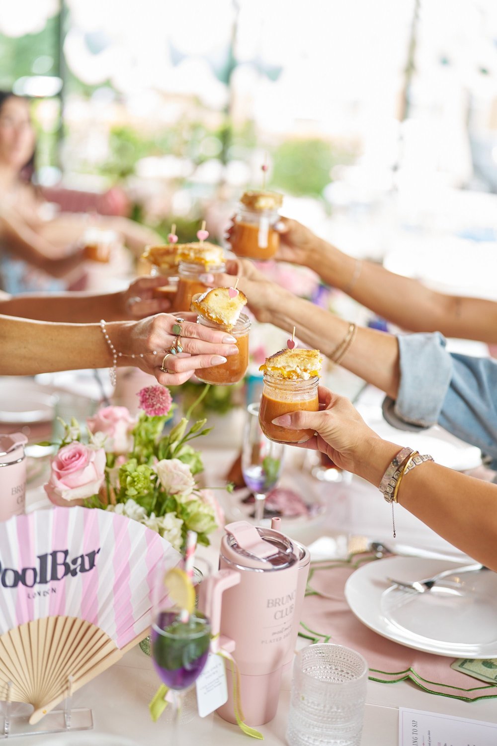 Friends clinking jars of a layered dessert over a floral table