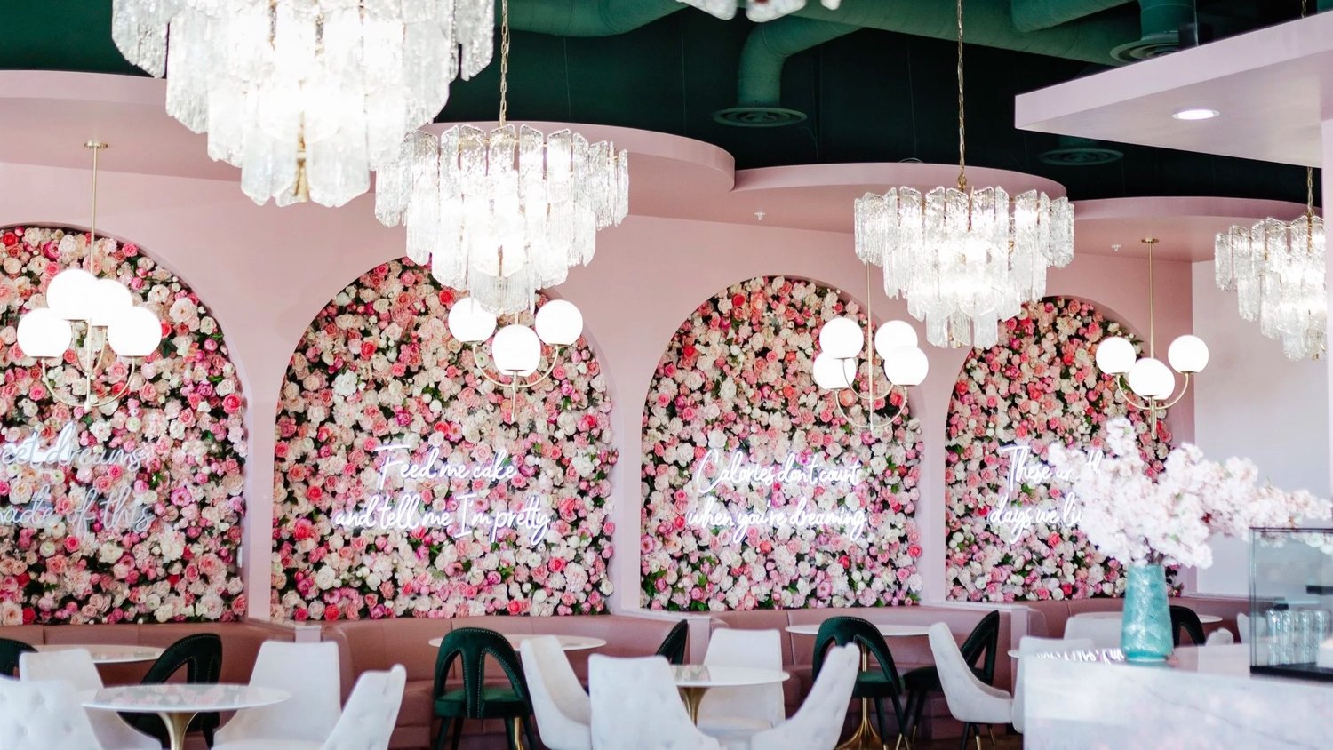 The Plated Dreams dining room: arched flower walls with neon script, crystal chandeliers and white marble tables