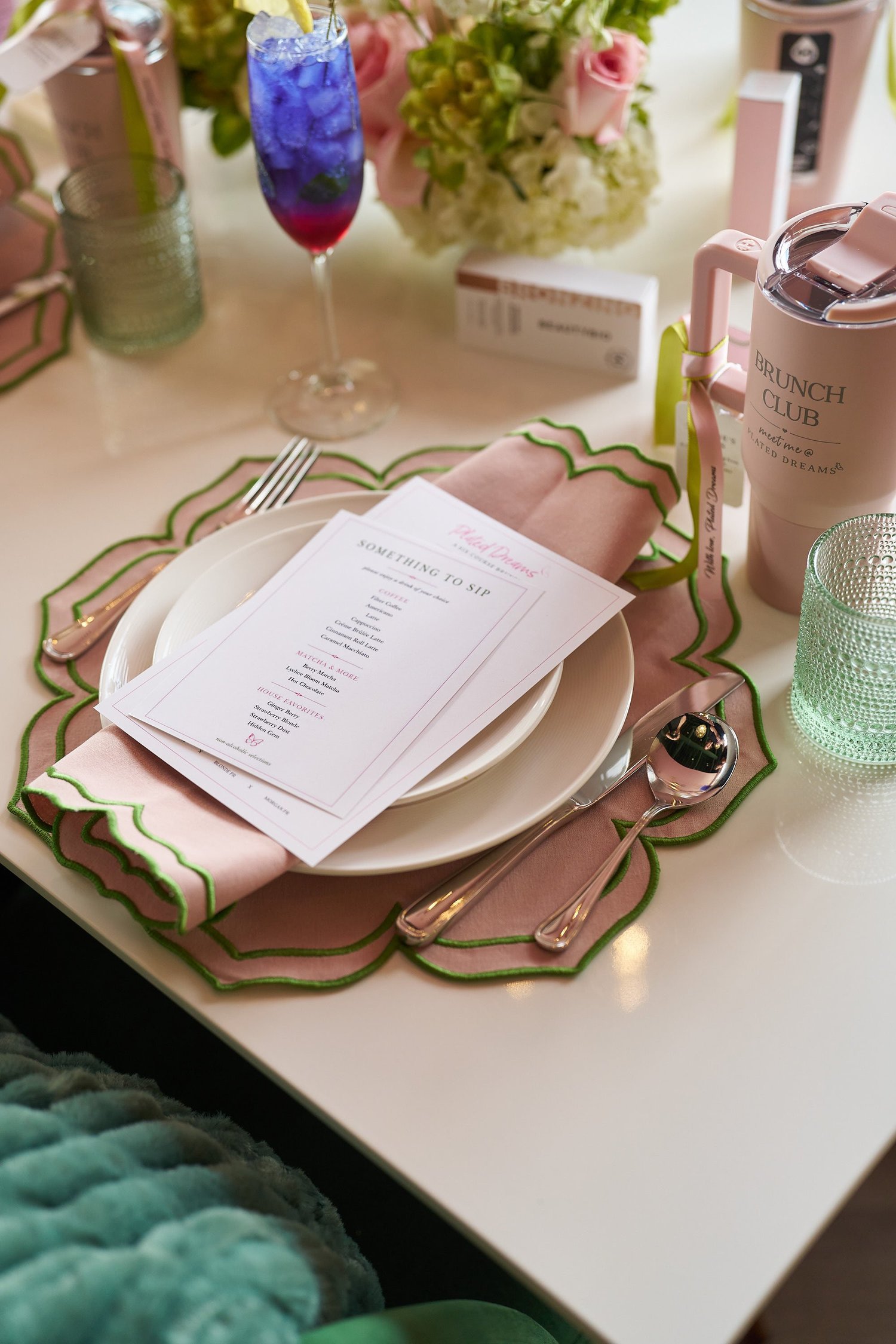 A set place with a printed menu, pink napkin and a violet cocktail